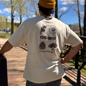 Man showing the back of the shirt, which says "Kind Coffee" and has botanical images around it 