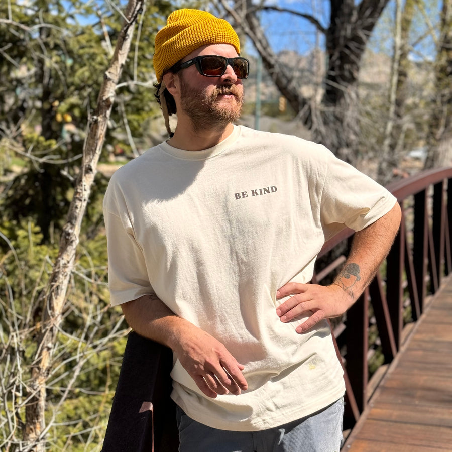 Man with sunglasses on and a t-shirt that says "Be Kind" on the upper left lapel 